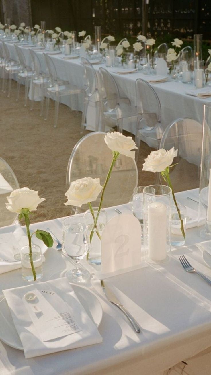 Elegant wedding reception table with white linens, place settings, water glasses, and white rose centerpieces in clear vases